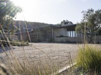 a house surrounded by lots of trees and a dirt road with rocks and grass surrounding it