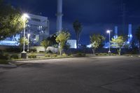 a night view looking at an empty street near several plants and trees with lights on