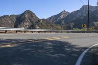 an open road with yellow lines next to mountains and trees on the side of it