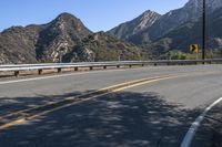 an open road with yellow lines next to mountains and trees on the side of it