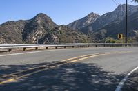 an open road with yellow lines next to mountains and trees on the side of it