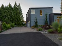 driveway leading to a grey house with blue siding, and trees in the background,