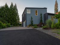 driveway leading to a grey house with blue siding, and trees in the background,