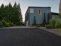 driveway leading to a grey house with blue siding, and trees in the background,