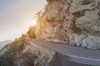 a car driving down an empty road along a cliff side in front of a sunrise