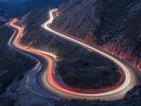 many lanes of curved road on the side of a mountain side at dusk with cars going along it