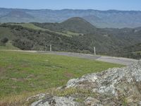 a person riding a bicycle on the side of a mountain road with mountains behind them