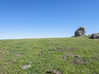 a hill top with large rocks and grass on the hill, surrounded by bright blue sky