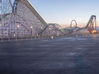 an empty area with a roller coaster and a tall structure in the background at dusk