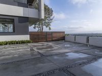 the concrete patio is surrounded by cement tiles with steel posts, a wooden privacy fence and greenery