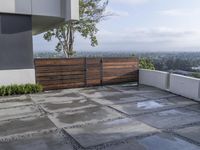 the concrete patio is surrounded by cement tiles with steel posts, a wooden privacy fence and greenery