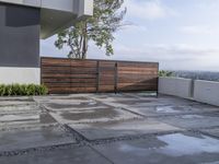 the concrete patio is surrounded by cement tiles with steel posts, a wooden privacy fence and greenery