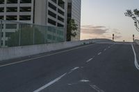 the street is empty near a large building at dusk and people riding a skateboard down it