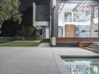 large concrete walkway alongside a modern modern house at night with glass railings and lighting on