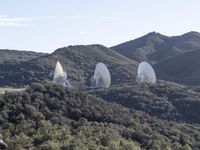 several radio telescopes on top of a hill near trees and mountains are being viewed