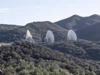 several radio telescopes on top of a hill near trees and mountains are being viewed