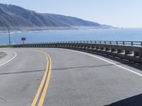 a motorcycle riding down the coast on an empty road with mountains in the background and blue waters