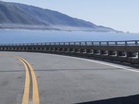 a motorcycle riding down the coast on an empty road with mountains in the background and blue waters