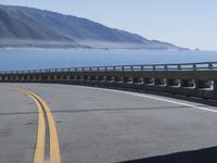 a motorcycle riding down the coast on an empty road with mountains in the background and blue waters