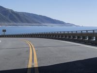 a motorcycle riding down the coast on an empty road with mountains in the background and blue waters