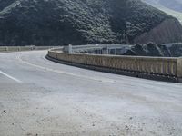 a woman riding a motorcycle down the side of a road next to a cliff slope