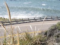 a man riding a bike near the ocean on the road and a surf board on a railing