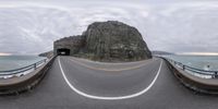 this is an image of a road going out to sea side by a rock in the distance