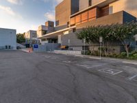 some people are walking in an empty parking lot near buildings with trees and a few concrete blocks