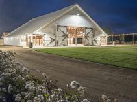 an old barn with plants and flowers surrounding it at night time, outside of the structure