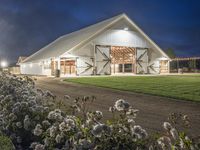 an old barn with plants and flowers surrounding it at night time, outside of the structure