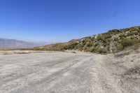 an empty road in the middle of nowhere with desert on the ground, and mountain peaks in the distance