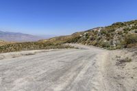 an empty road in the middle of nowhere with desert on the ground, and mountain peaks in the distance