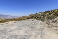 an empty road in the middle of nowhere with desert on the ground, and mountain peaks in the distance