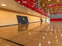 an empty basketball court with a red and white wall and wood flooring is shown