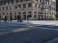 a group of people walking across an intersection on a sunny day wearing jackets and hats