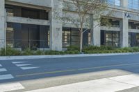 a car driving down a street past tall buildings and trees on a street corner in front of a curb