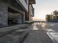 the entrance to an empty brick building in a town at sunset and driveway with stairs up to two cars parked on a street