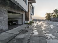 the entrance to an empty brick building in a town at sunset and driveway with stairs up to two cars parked on a street