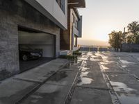 the entrance to an empty brick building in a town at sunset and driveway with stairs up to two cars parked on a street