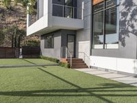 the lawn outside the two story modern home is lined with fake grass and some stairs