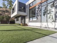 the lawn outside the two story modern home is lined with fake grass and some stairs