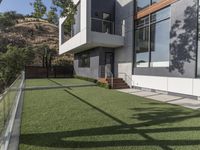 the lawn outside the two story modern home is lined with fake grass and some stairs