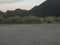 a bike rests on a gravel road near mountains on a sunny day with sky at the back