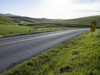 a view of the winding road leading to green hills and grass on both sides of the road