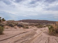 a dirt road that goes through the desert in the daytime time as a cloudy sky is over