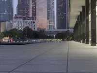 the walkway at the park leads to a lake and buildings in the background as evening falls