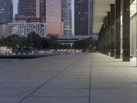 the walkway at the park leads to a lake and buildings in the background as evening falls