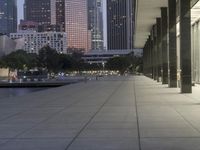 the walkway at the park leads to a lake and buildings in the background as evening falls