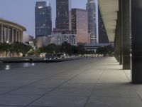 the walkway at the park leads to a lake and buildings in the background as evening falls