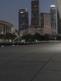 the walkway at the park leads to a lake and buildings in the background as evening falls